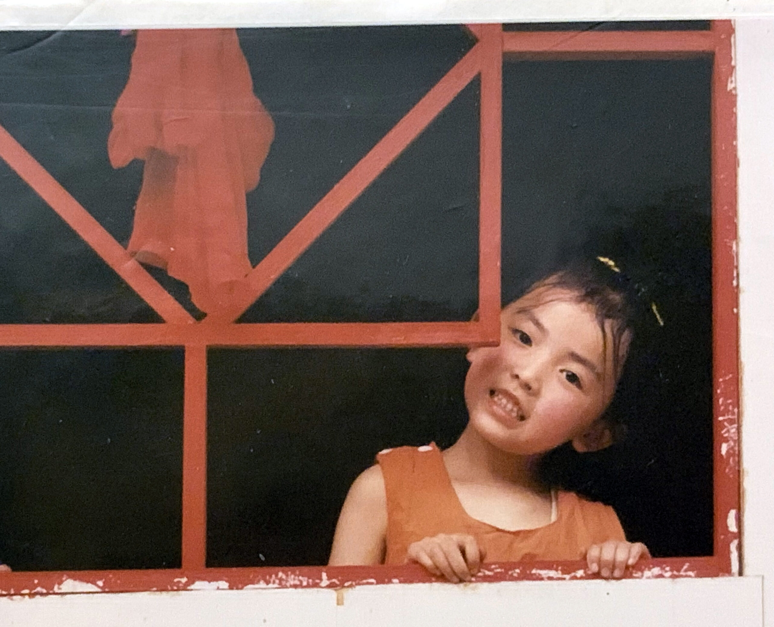 A young girl looks through a red window.